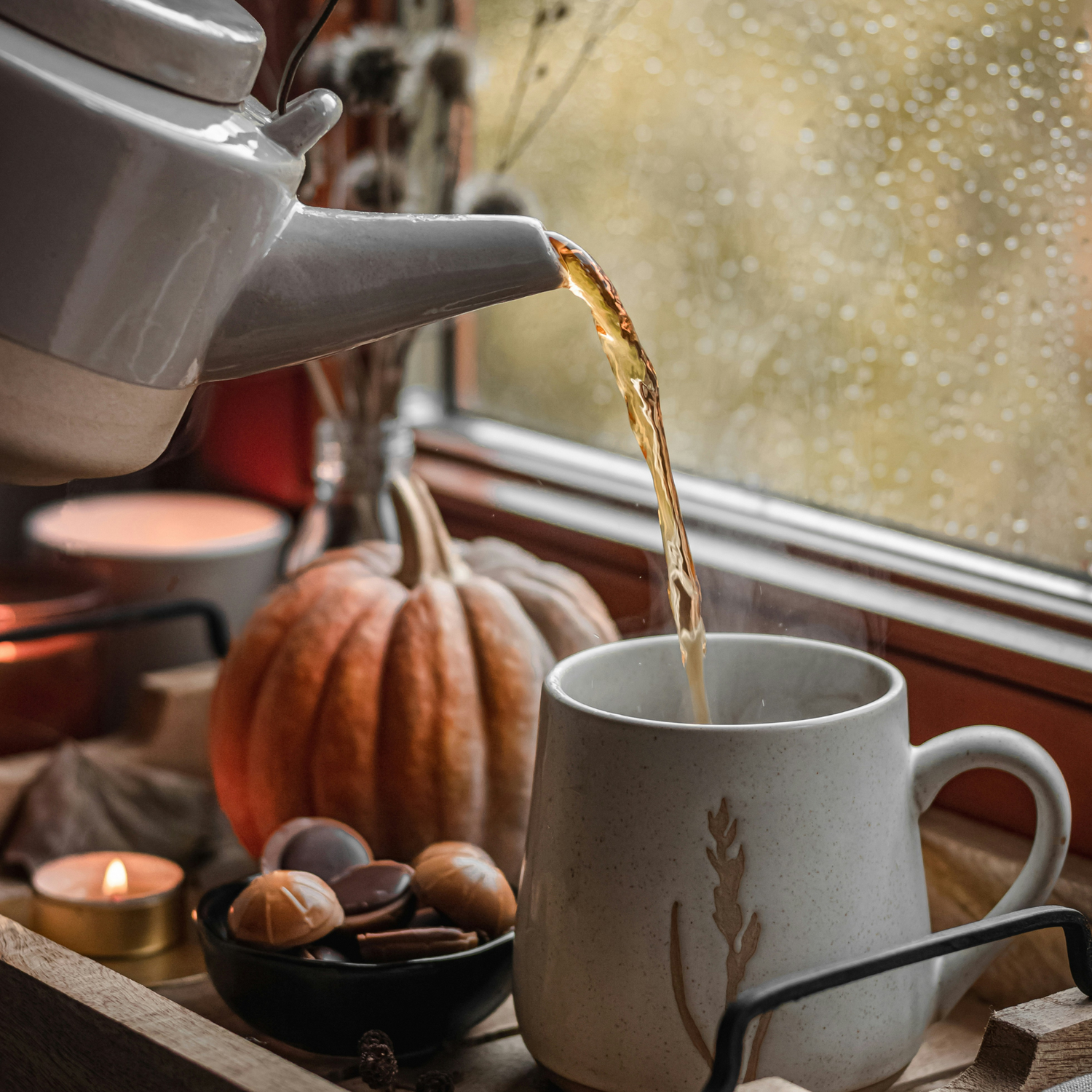 Tea being poured from a teapot into a mug with a pumpkin and candles in the background.