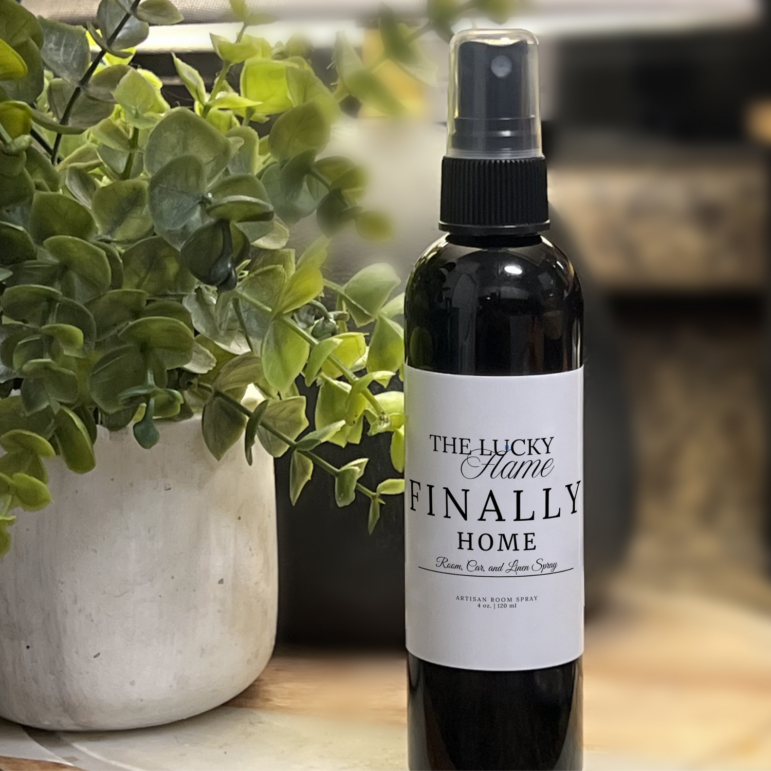 Finally Home room, linen, and car spray with eucalyptus and mint in a sleek 4 oz black bottle styled with white towels, eucalyptus sprigs, and spa-like elements.