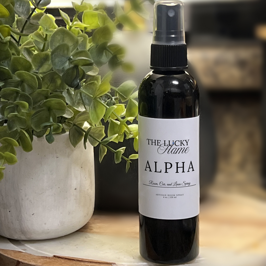 Alpha room, linen, and car spray in a sleek 4 oz black bottle with notes of coconut, oakmoss, and sandalwood, styled with wood accents and a clean, masculine vibe.