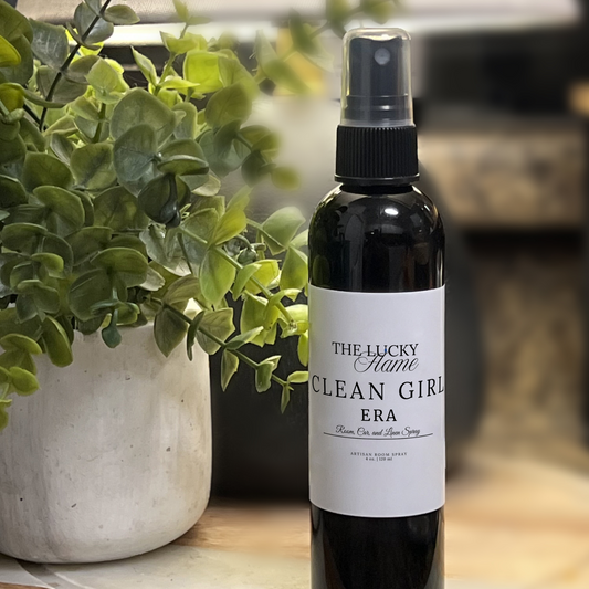 Girl Era room, linen, and car spray in a sleek 4 oz black bottle with anise, soft powder, and sandalwood notes styled with light fabrics and minimal beauty accessories.