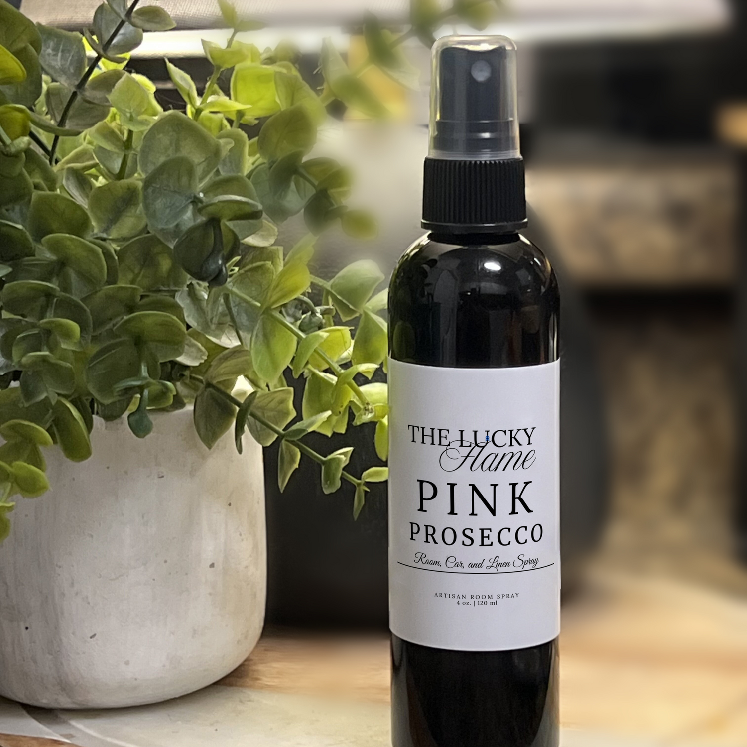 Pink Prosecco room, linen, and car spray in a sleek 4 oz black bottle with notes of peach, sugar, and sandalwood, styled with bubbly, feminine details and soft lighting.