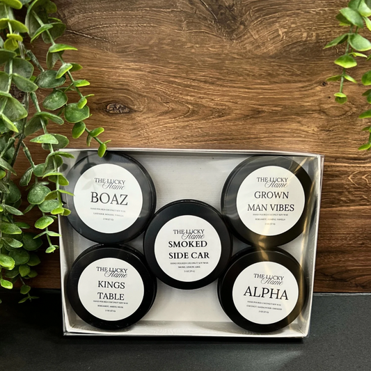 Masculine Candle Discovery Set with five 2 oz black tins (Boaz, King’s Table, Alpha, Smoked Side Car, Grown Man Vibes) in a clear gift box on a wood backdrop.